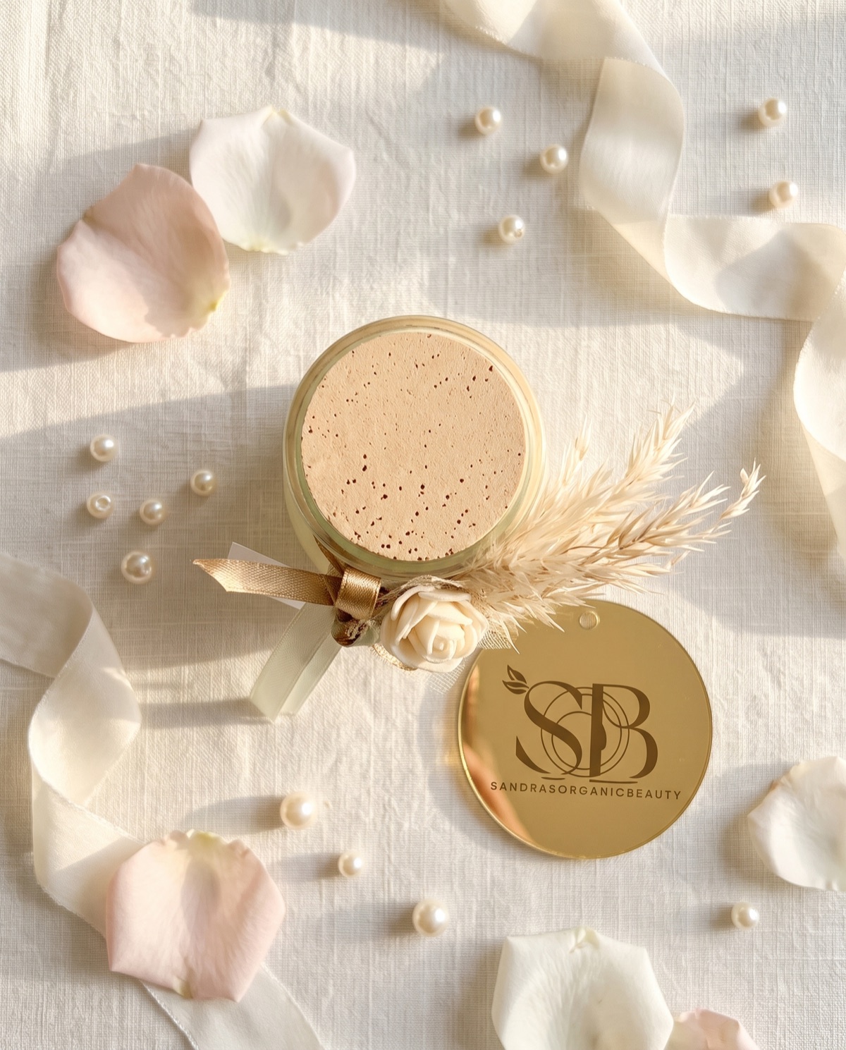The cork jar candle from above with pampas, a cream rose and its gold mirror tag on linen