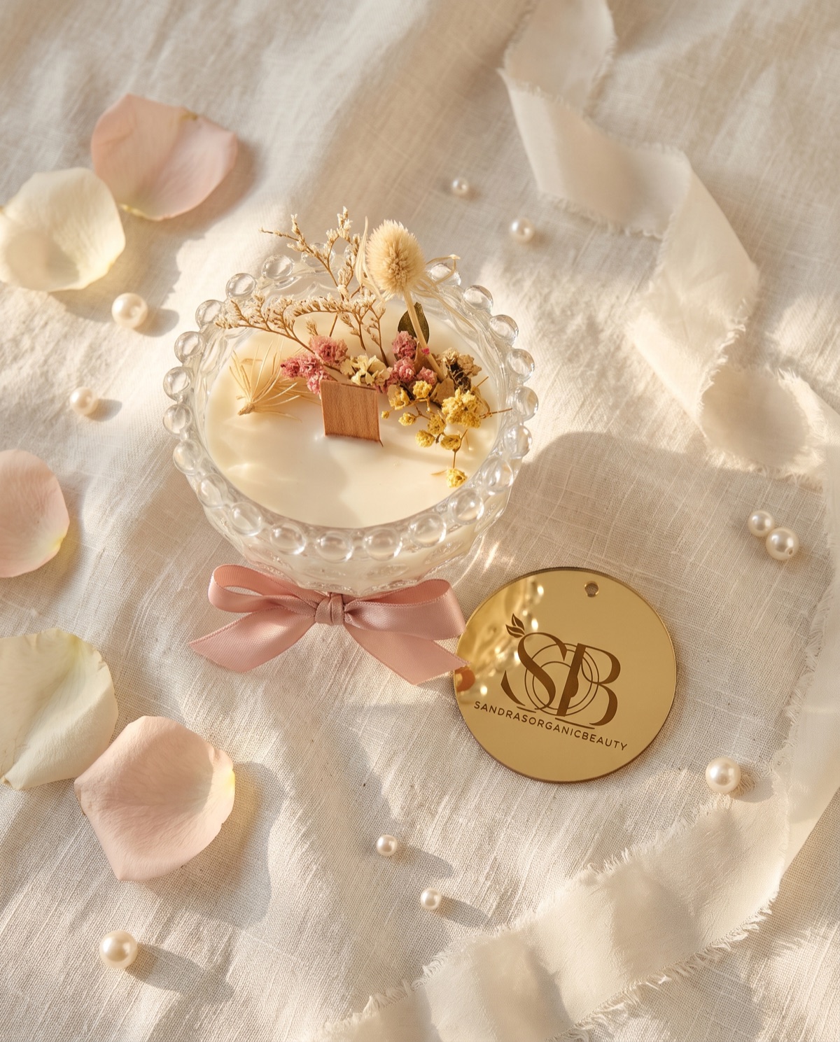 The dried flower bowl candle from above with its gold mirror tag, petals and pearls on linen